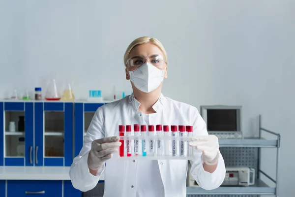 Scientist in goggles and white coat holding test tubes with monkeypox lettering in lab - foto de stock