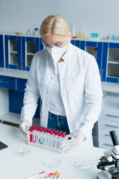 Scientist holding test tubes with monkeypox lettering near microscope in lab — Stock Photo