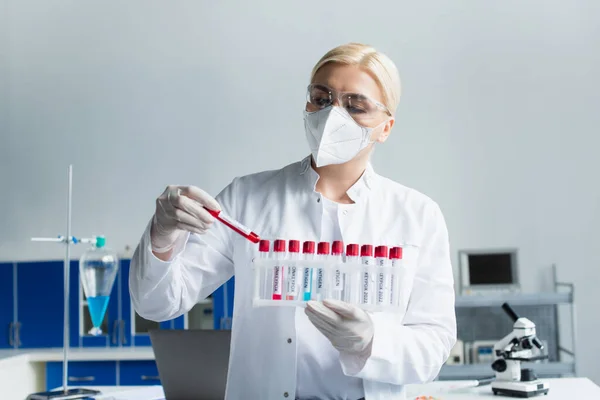 Researcher in protective mask holding test tubes with monkeypox lettering in laboratory — Stock Photo