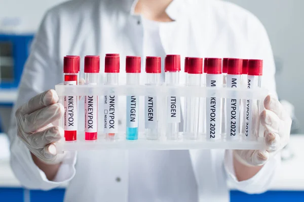 Ausgeschnittene Ansicht eines Wissenschaftlers in Latexhandschuhen, der Reagenzgläser mit Affenpocken-Schriftzug im Labor hält — Stockfoto