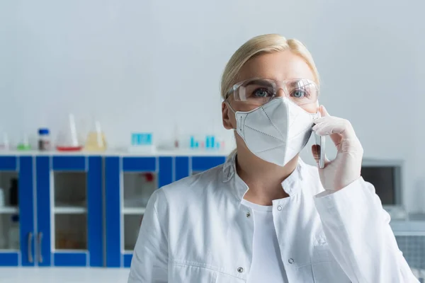 Scientist in goggles and protective mask talking on smartphone in lab — Stock Photo