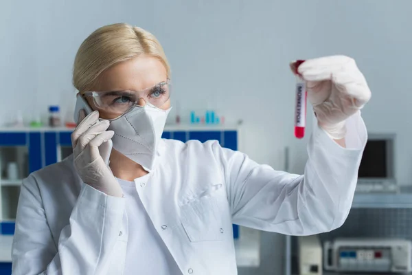 Cientista em óculos falando no smartphone e olhando para tubo de teste em laboratório — Fotografia de Stock