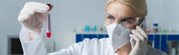 Wissenschaftler in Schutzmaske spricht auf Smartphone und hält verschwommenes Reagenzglas im Labor, Banner — Stockfoto