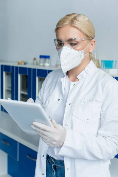 Cientista em máscara protetora e óculos usando tablet digital em laboratório — Fotografia de Stock