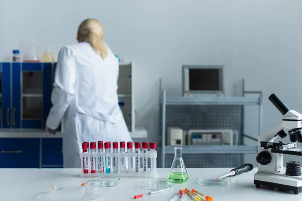 Visão traseira do cientista trabalhando perto de tubos de ensaio com letras de varíola e microscópio em laboratório — Fotografia de Stock