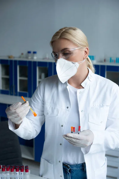 Scientist in protective goggles holding syringes near test tubes in lab — Stock Photo