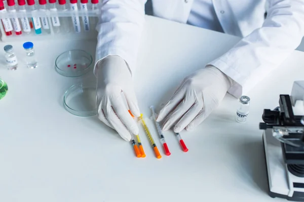 Vista cultivada do cientista em luvas de látex segurando seringas perto de tubos de ensaio e vacinas em laboratório — Fotografia de Stock