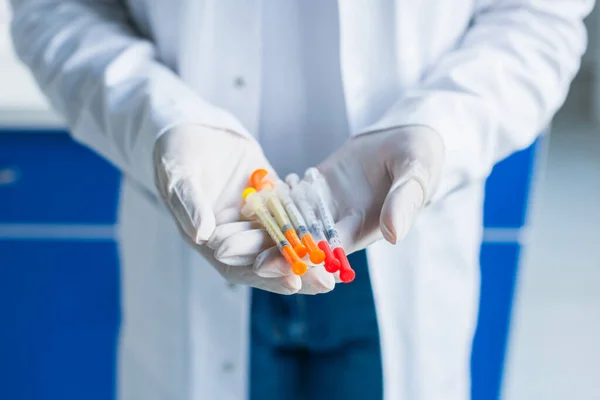 Cropped view of scientist in latex gloves holding syringes in lab — стоковое фото