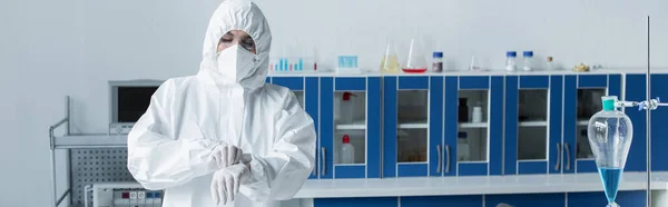 Cientista em terno hazmat usando luvas de látex no laboratório, banner — Fotografia de Stock