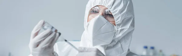 Scientist in protective suit and mask holding syringe and vaccine in lab, banner — стоковое фото