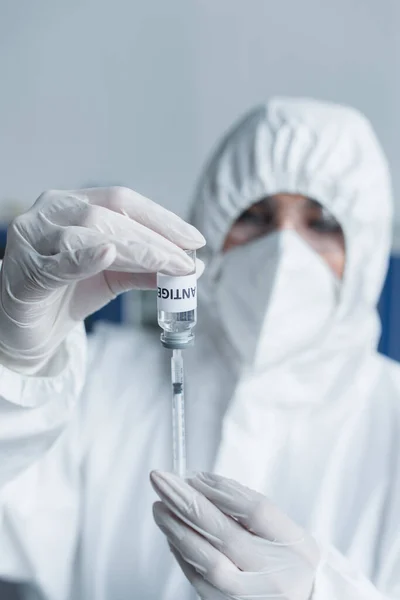 Blurred scientist in latex gloves holding antigen and syringe in laboratory — стоковое фото