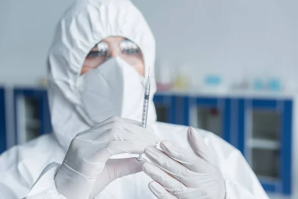 Blurred scientist in hazmat suit holding syringe in laboratory — Stockfoto