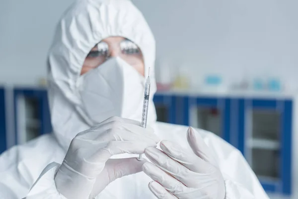 Blurred scientist in hazmat suit holding syringe in laboratory — Fotografia de Stock