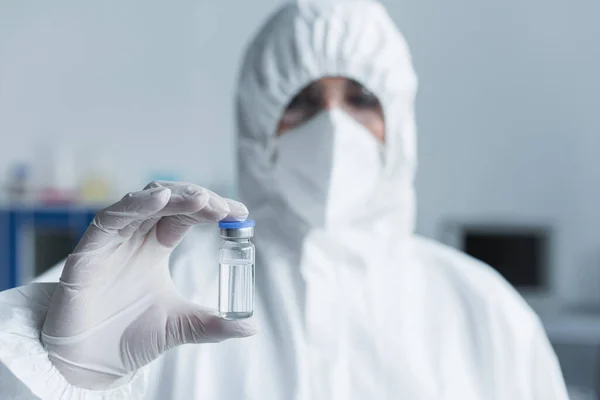 Розмитий вчений у костюмі ризику, що тримає вакцину в лабораторії — стокове фото