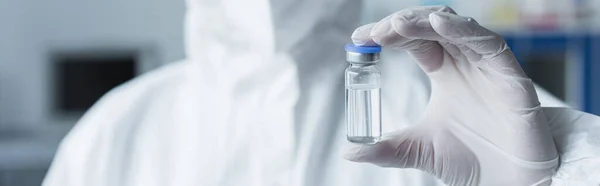 Обрезанный вид ученого в защитном костюме и латексной перчатке с вакциной в лаборатории, баннер — стоковое фото