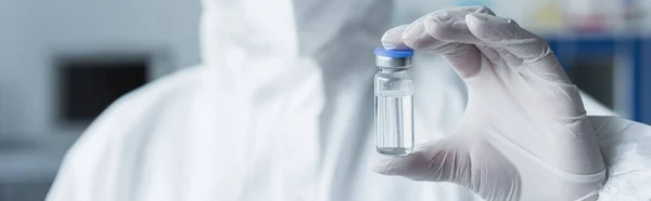 Cropped view of scientist in hazmat suit and latex glove holding vaccine in lab, banner — Stock Photo