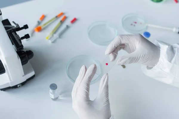 Cropped view of scientist holding glass near petri dishes and microscope in lab — Stock Photo