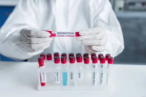 Cropped view of scientist in hazmat suit holding test tube with monkeypox lettering in lab — Photo de stock