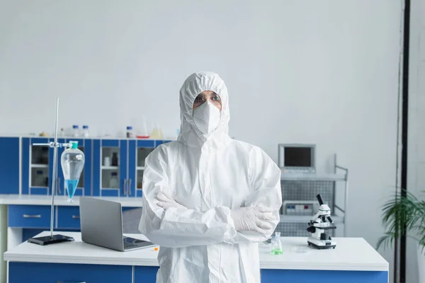 Scientist in hazmat suit and protective goggles crossing arms in lab — Stock Photo