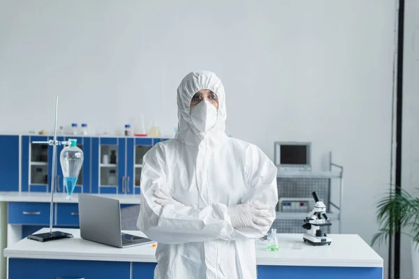 Scientist in hazmat suit and protective goggles crossing arms in lab — стоковое фото