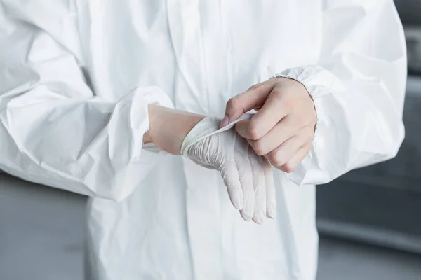 Ausgeschnittene Ansicht eines Wissenschaftlers im Schutzanzug, der im Labor den Latexhandschuh auszieht — Stockfoto