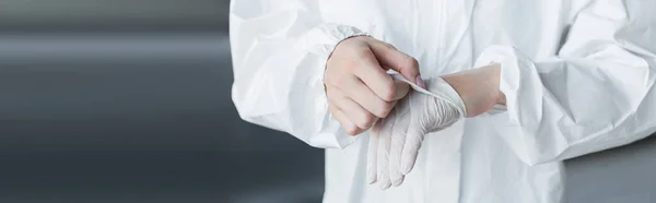 Ausgeschnittene Ansicht eines Wissenschaftlers im Schutzanzug, der im Labor den Latexhandschuh auszieht, Banner — Stockfoto