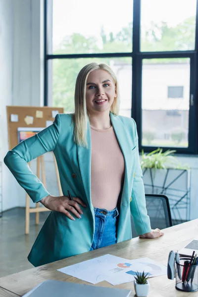 Psicólogo sorrindo olhando para a câmera perto de papéis na mesa na sala de consulta — Fotografia de Stock