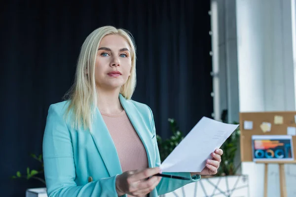 Psychologist looking at camera while holding paper in consultation room - foto de stock