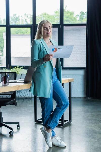 Smiling psychologist holding paper near laptop on table in consultation room — Fotografia de Stock