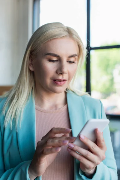 Blonde psychologist using mobile phone in consultation room — Stock Photo