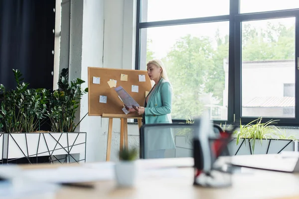 Side view of psychologist holding paper near board in consulting room — Foto stock