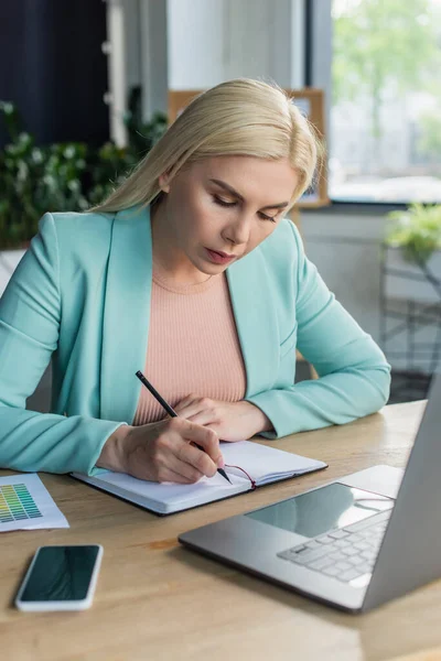 Psychologist writing on notebook near devices in consultation room - foto de stock