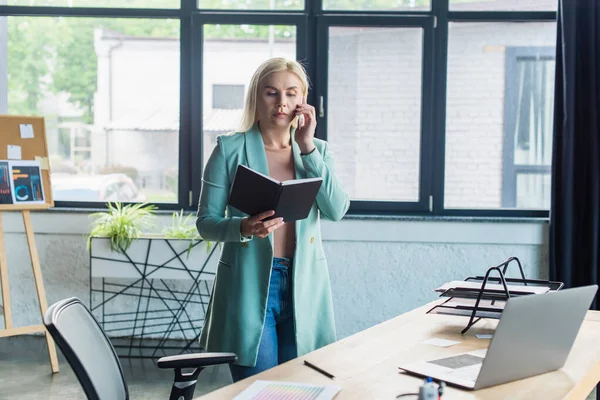 Psychologist looking at notebook and talking on smartphone in consultation room - foto de stock