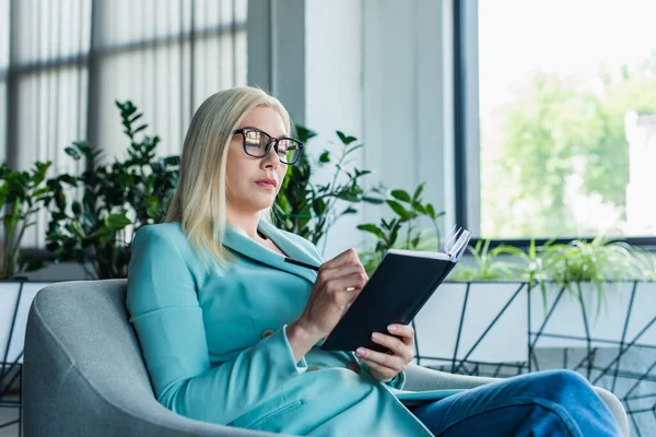 Psychologist writing on notebook on armchair in consultation room - foto de stock