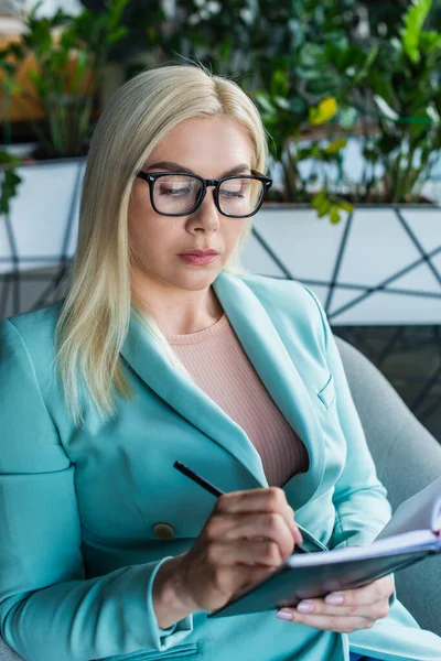 Psychologist in eyeglasses writing on notebook in consultation room — стоковое фото