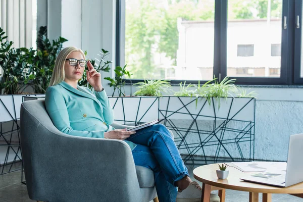 Psychologe mit Brille hält Notizbuch in der Hand, während er im Sprechzimmer auf einem Sessel sitzt — Stockfoto