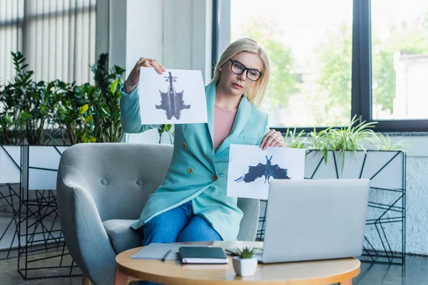 Psychologist holding Rorschach test during video call on laptop near notebook in consultation room — Stock Photo