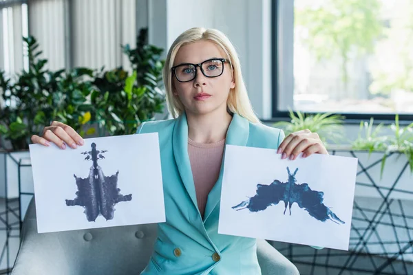 Psychologist in eyeglasses holding Rorschach test and looking at camera in consultation room — Stock Photo