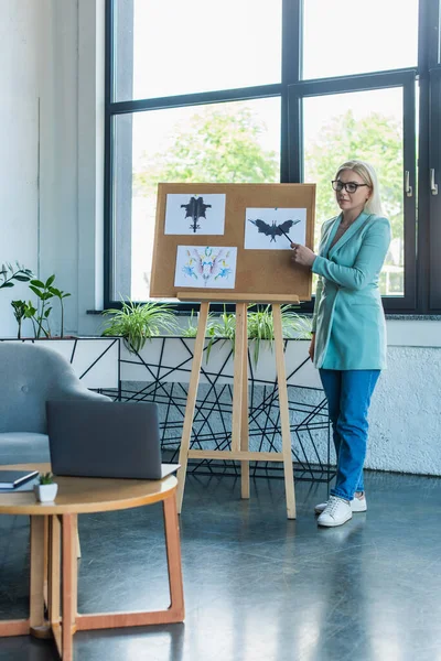 Psychologist pointing at Rorschach test on board during video call on laptop in consultation room — Photo de stock