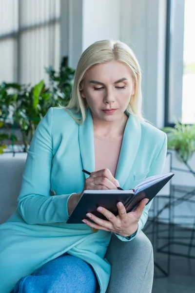 Psychologe schreibt auf Notizbuch auf Sessel im Beratungszimmer — Stockfoto