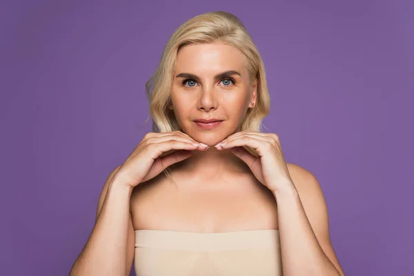 Blonde woman with bare shoulders and blue eyes looking at camera isolated on purple — Stock Photo