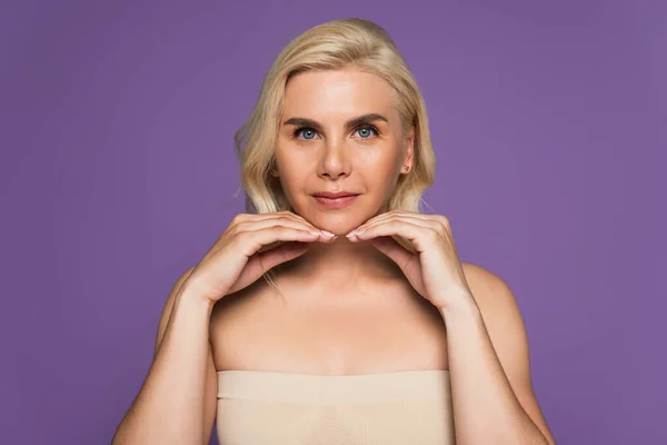 Blonde woman with bare shoulders and blue eyes looking at camera isolated on purple — Foto stock