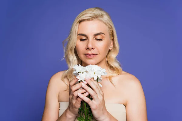 Блондинка с голыми плечами, смотрящая на белые цветы, изолированные на фиолетовой — стоковое фото