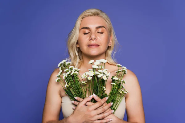 Blonde woman with closed eyes smelling flowers isolated on purple — Fotografia de Stock