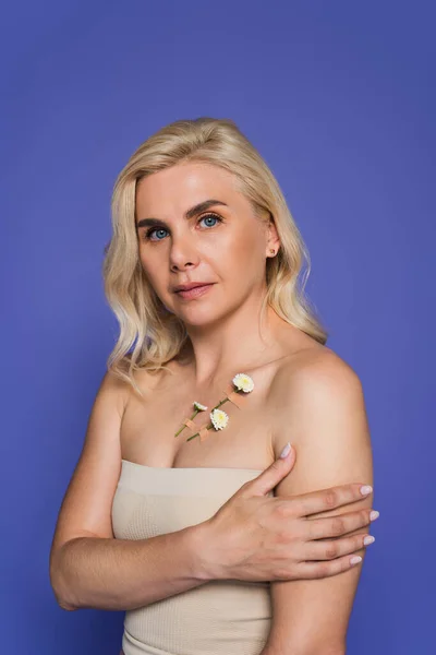 Blonde woman with plasters and blooming flowers on body looking at camera isolated on purple — Stock Photo