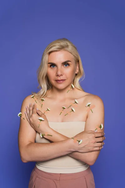 Blonde woman with plasters and fresh flowers on body looking at camera isolated on purple — Photo de stock