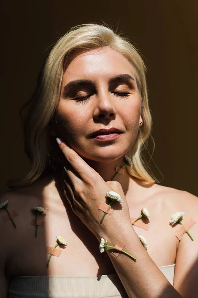 Sunshine on face of sensual blonde woman with closed eyes and blooming flowers on body isolated on black — Stock Photo