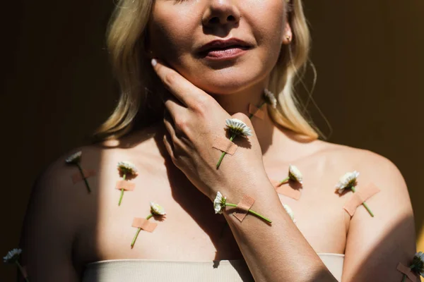 Vista recortada de mujer rubia con yeso y flores blancas en el cuerpo aislado en negro - foto de stock