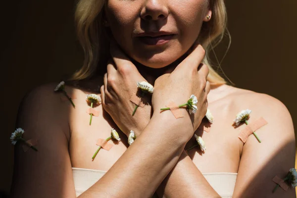 Cropped view of woman with with plasters and white flowers on body isolated on black - foto de stock