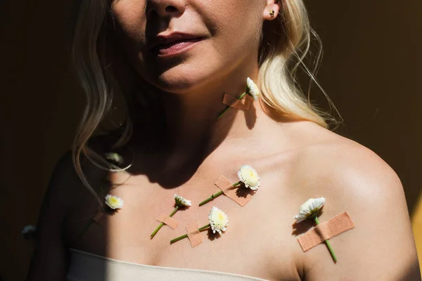 Partial view of woman with with plasters and white flowers on body isolated on black — Stock Photo